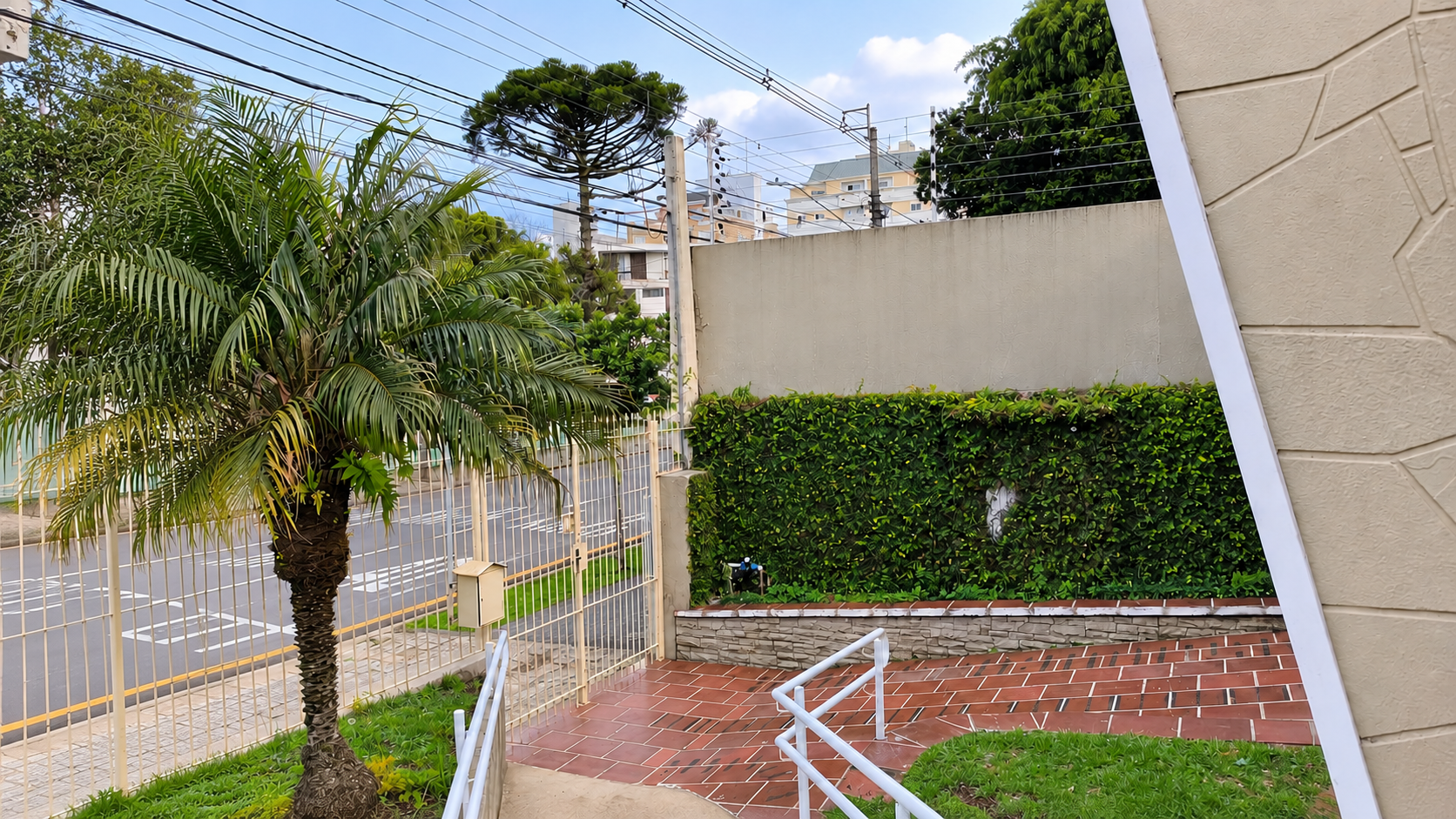 Área externa da Tenerezza, com vegetação, portão e caminho com corrimão.